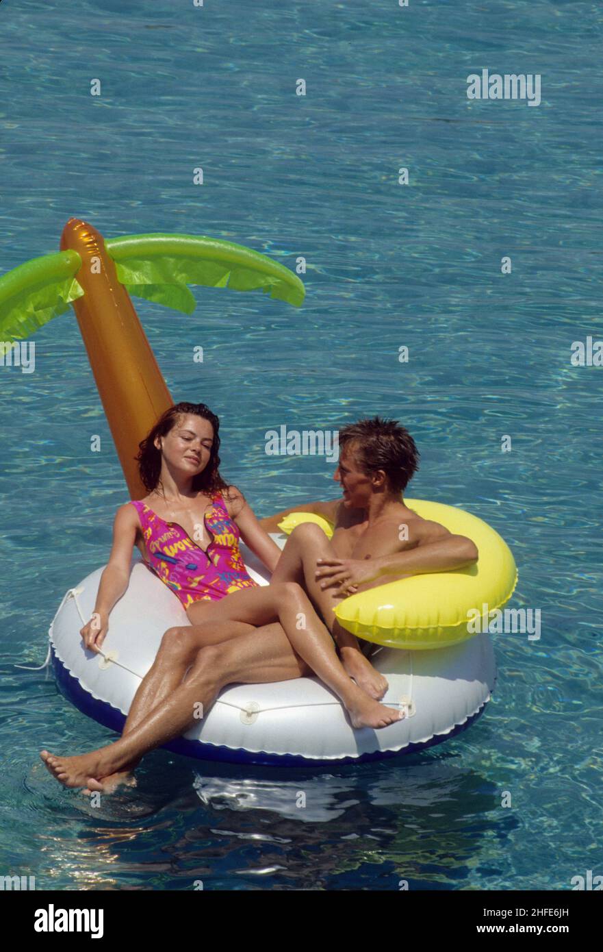 amorosa pareja joven colóchese colchón de plástico flotante sobre aguas claras de mar vacaciones de verano Foto de stock