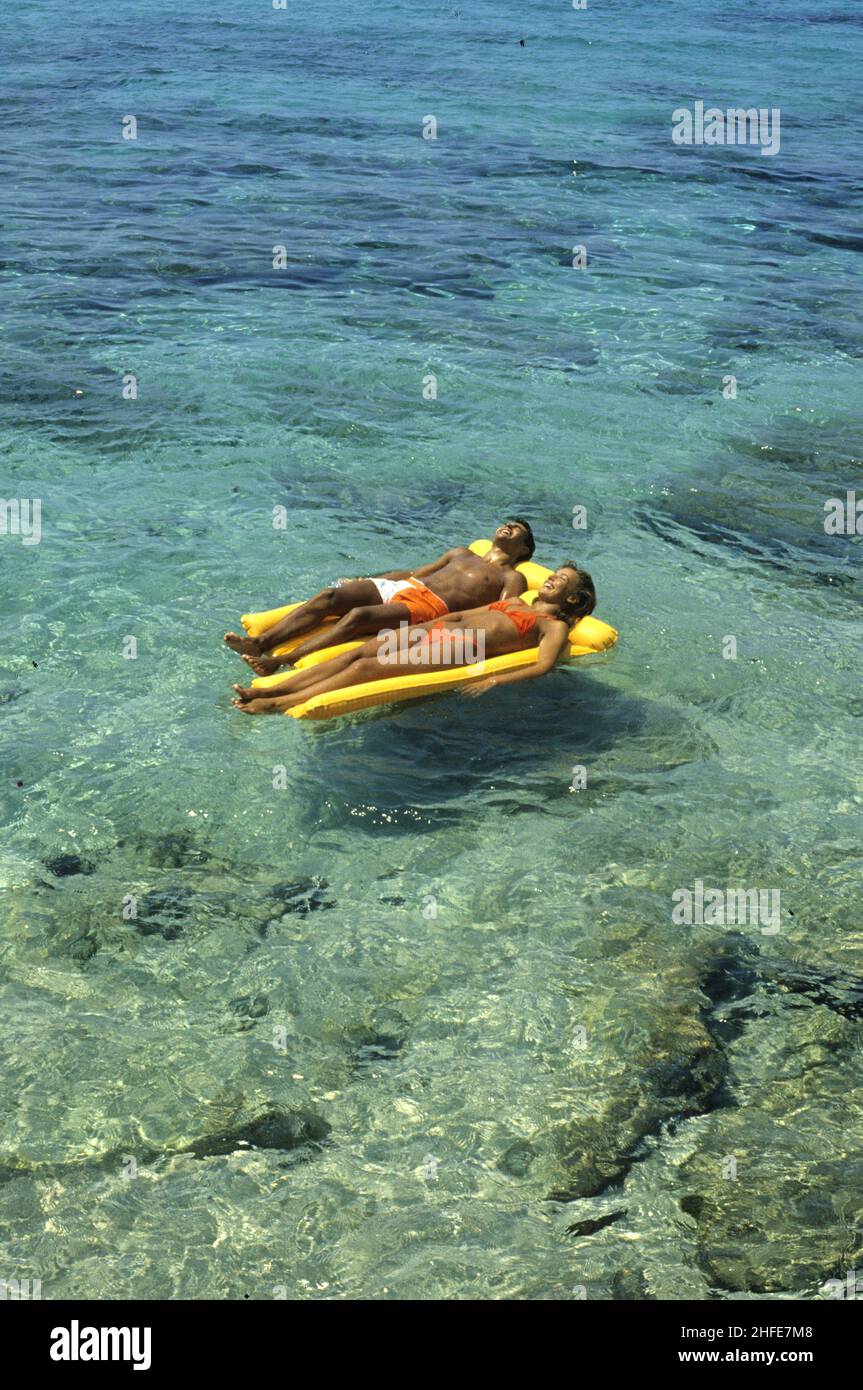 amorosa pareja joven colóchese colchón de plástico flotante sobre aguas claras de mar vacaciones de verano Foto de stock