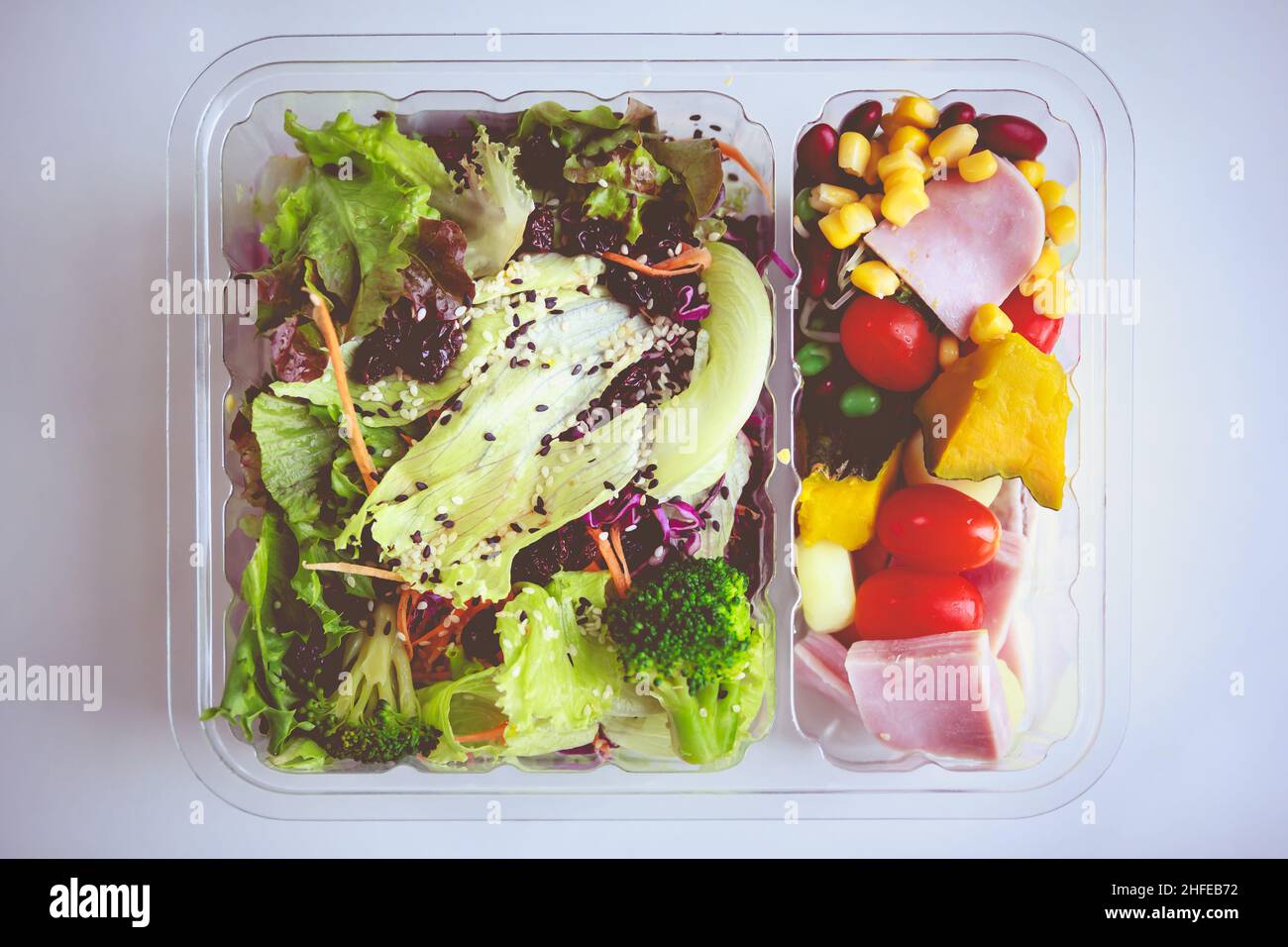 Ensalada de verduras mezcladas en envases de plástico sobre fondo blanco. Ensalada fresca para una buena salud. Concepto de alimentos saludables. Tono vintage. Foto de stock