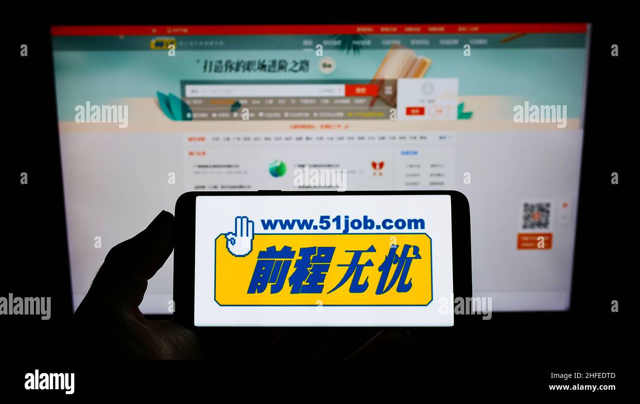 Persona que sostiene un smartphone con el logotipo de la empresa china de recursos humanos 51job Inc. En la pantalla frente al sitio web. Enfoque en la pantalla del teléfono. Foto de stock
