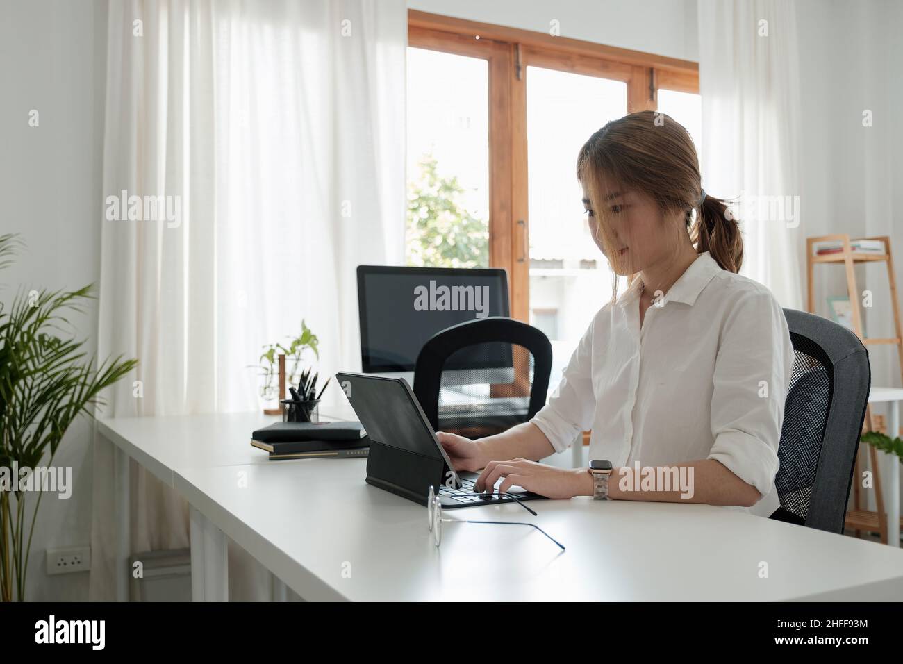 Una joven asiática trabaja en una tableta digital para aprender un curso o entrenamiento educativo, seminario, educación en línea en el concepto de casa Foto de stock