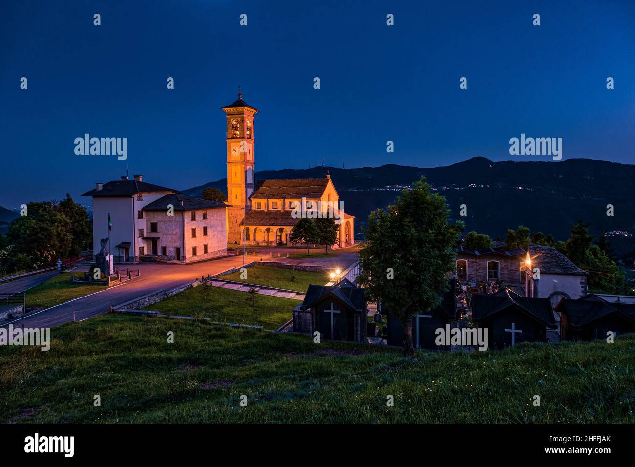 La iglesia local de Fuipiano Chiesa di San Giovanni Battista iluminada por la noche, rodeando colinas en la distancia. Foto de stock