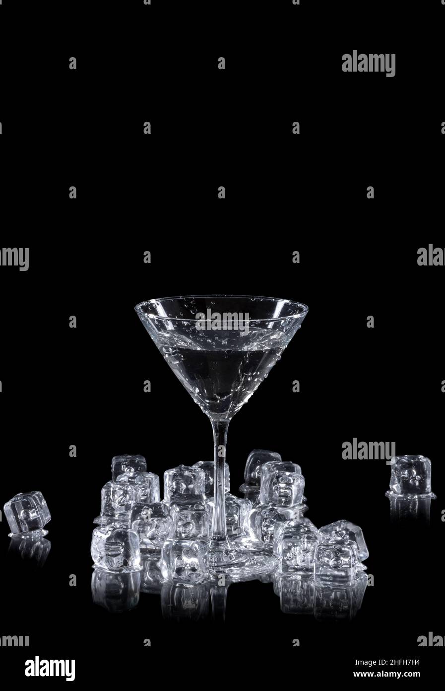 un cristal de martini rodeado de cubitos de hielo sobre un fondo negro reflectante, con espacio de copia Foto de stock