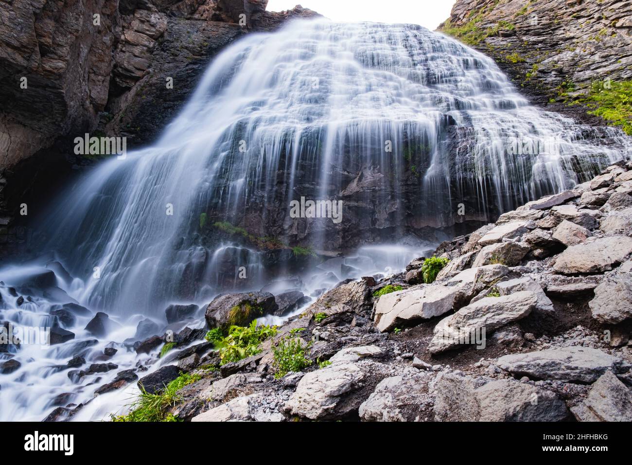 Una cascada gigante de montaña En un soleado día de verano, arroyos de agua caen desde una gran altura sobre rocas rocosas Foto de stock