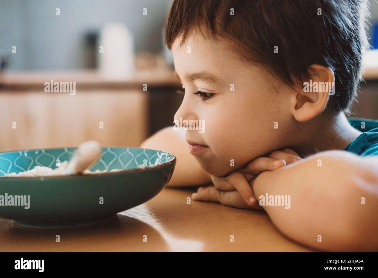 Niño con su cabeza descansando en la mesa y preguntándose si comer o no la gachas. Foto de stock