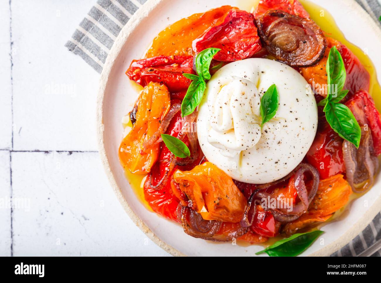 Queso burrata con tomates horneados, pimienta, cebolla roja y albahaca fresca sobre fondo blanco azulejo. Comida tradicional italiana. Vista superior. Primer plano. Foto de stock