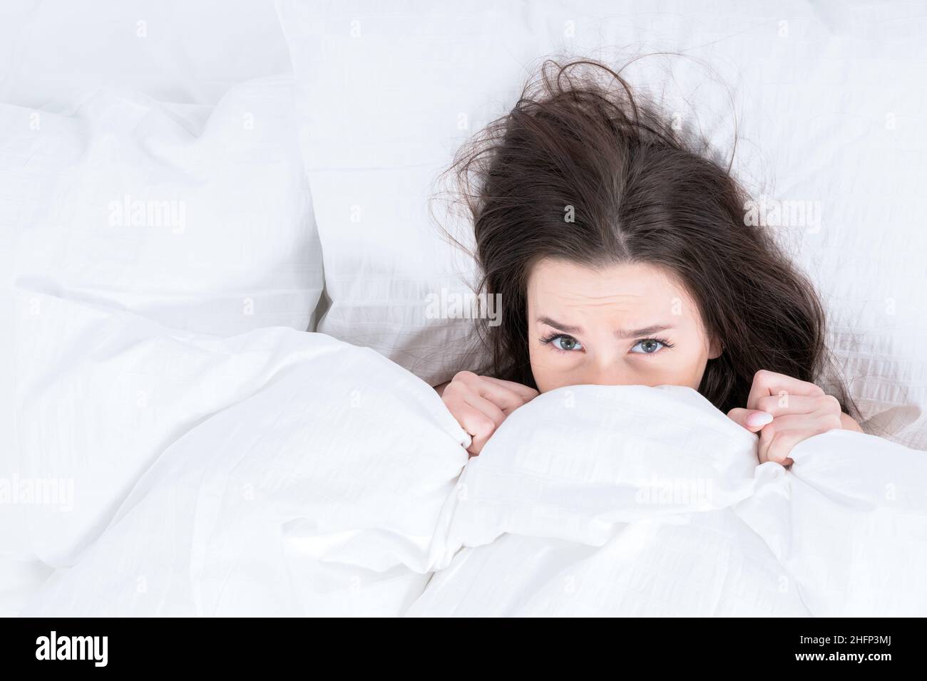 La niña se arrastró bajo el velo con su cuerpo, sólo su cabeza es visible. La morena se encuentra en la cama, calentándose en una mañana de invierno. Despertarse a distancia Foto de stock