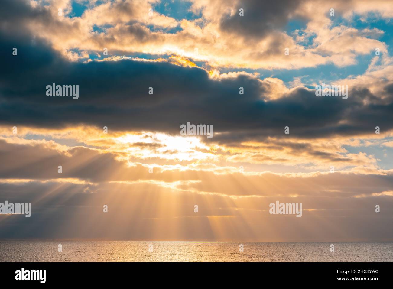 Poniendo rayos de sol que emanan a través de hermosas nubes sobre el agua Foto de stock