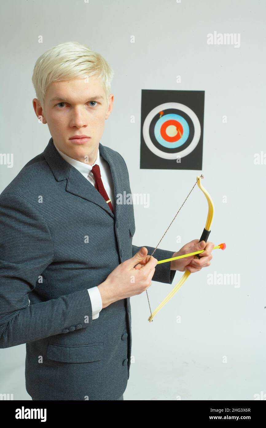 Hombre joven sosteniendo arco y tiro con arco blanco en el fondo. Foto de stock