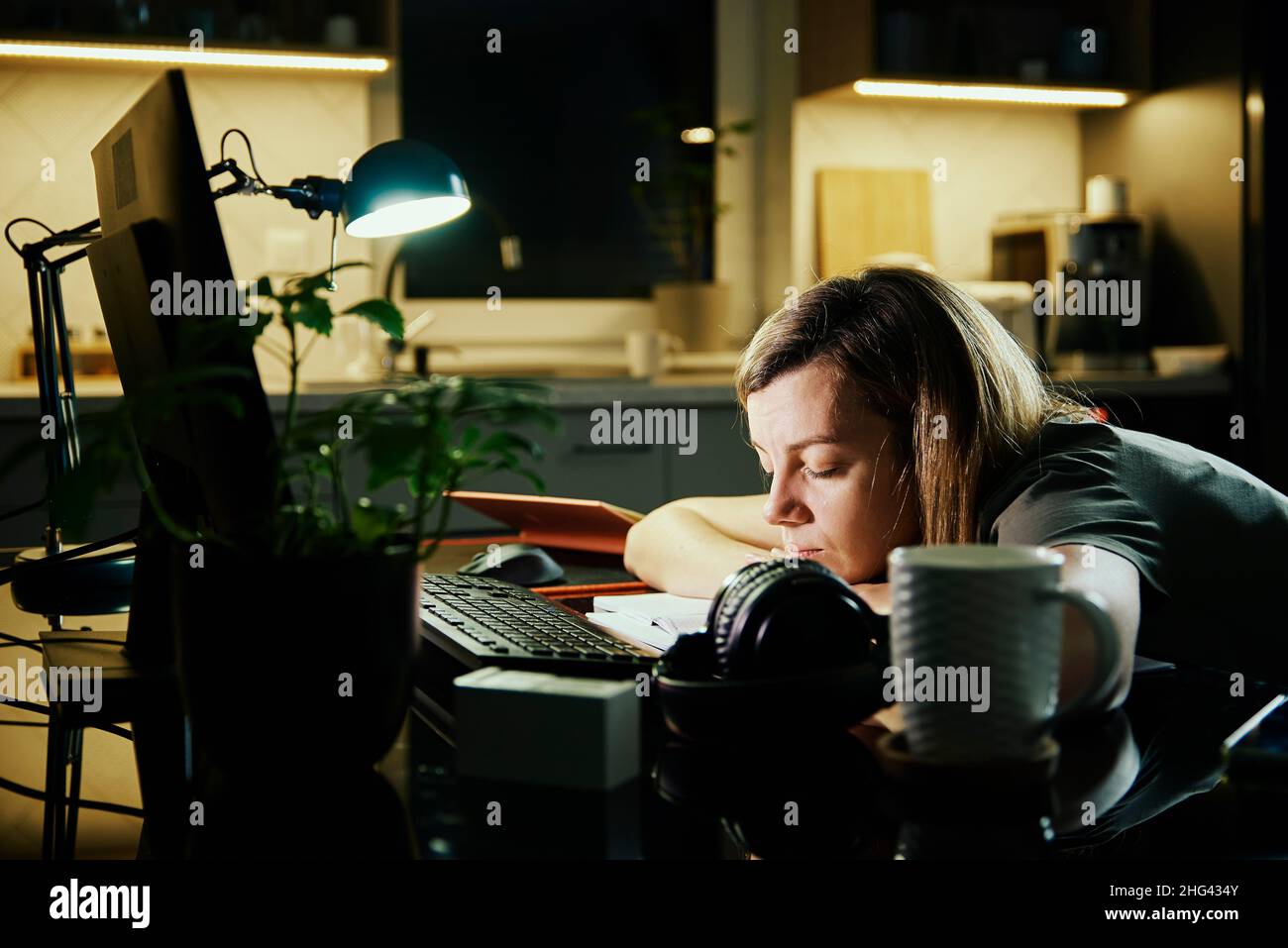 La mujer cansada trabaja desde la computadora del uso casero en la noche,  el agotamiento del trabajo excesivo, el freelancer trabaja remoto en el  lugar de trabajo casero Fotografía de stock -