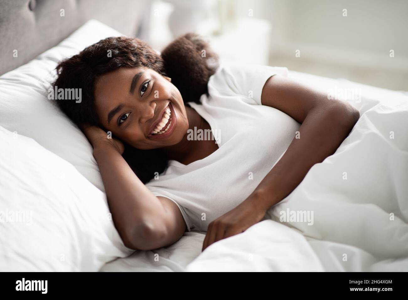 Foto de primer plano de la feliz dama negra bonita tumbada en la cama Foto de stock