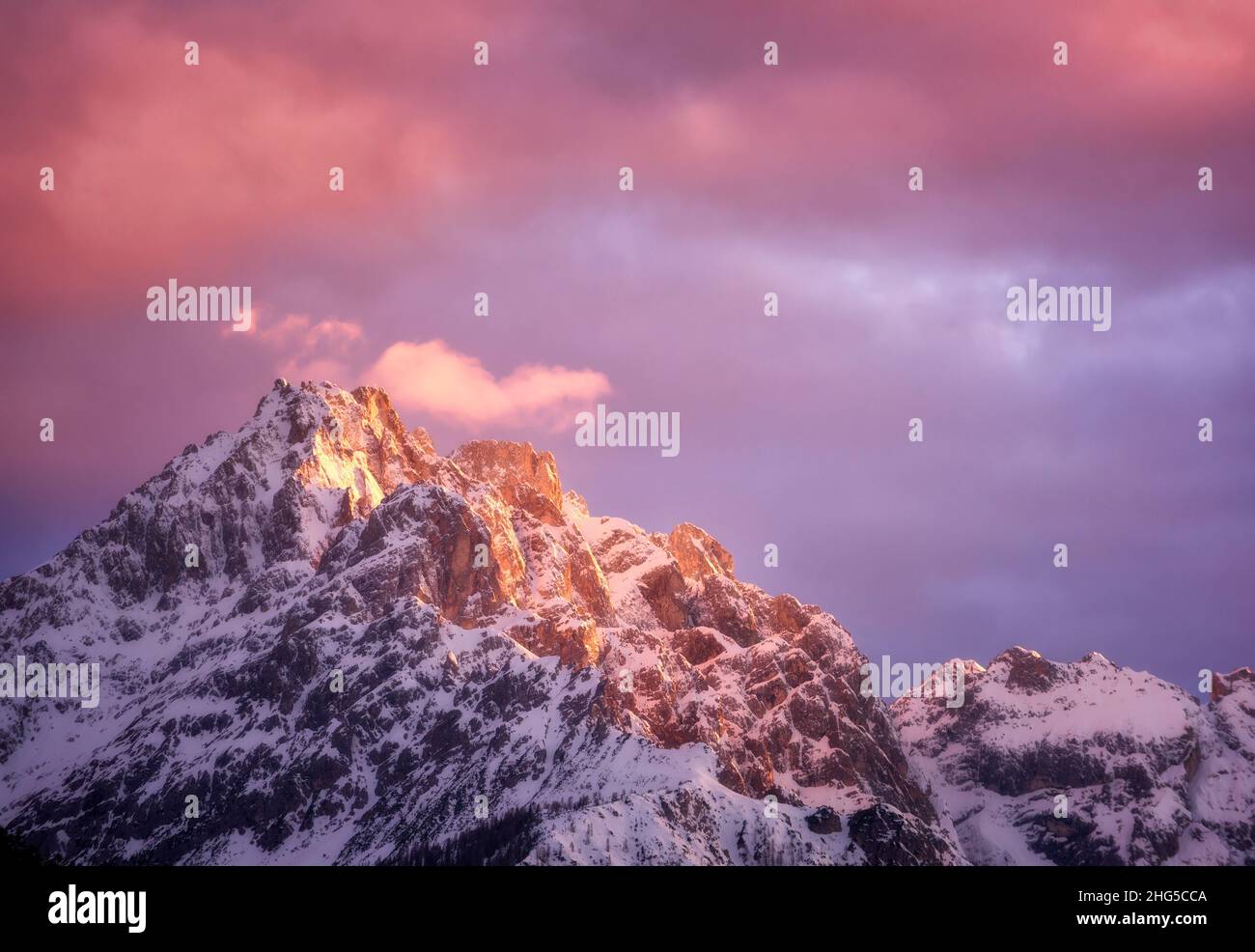 Hermosos picos montañosos en la nieve y el cielo violeta con nubes rosadas Foto de stock