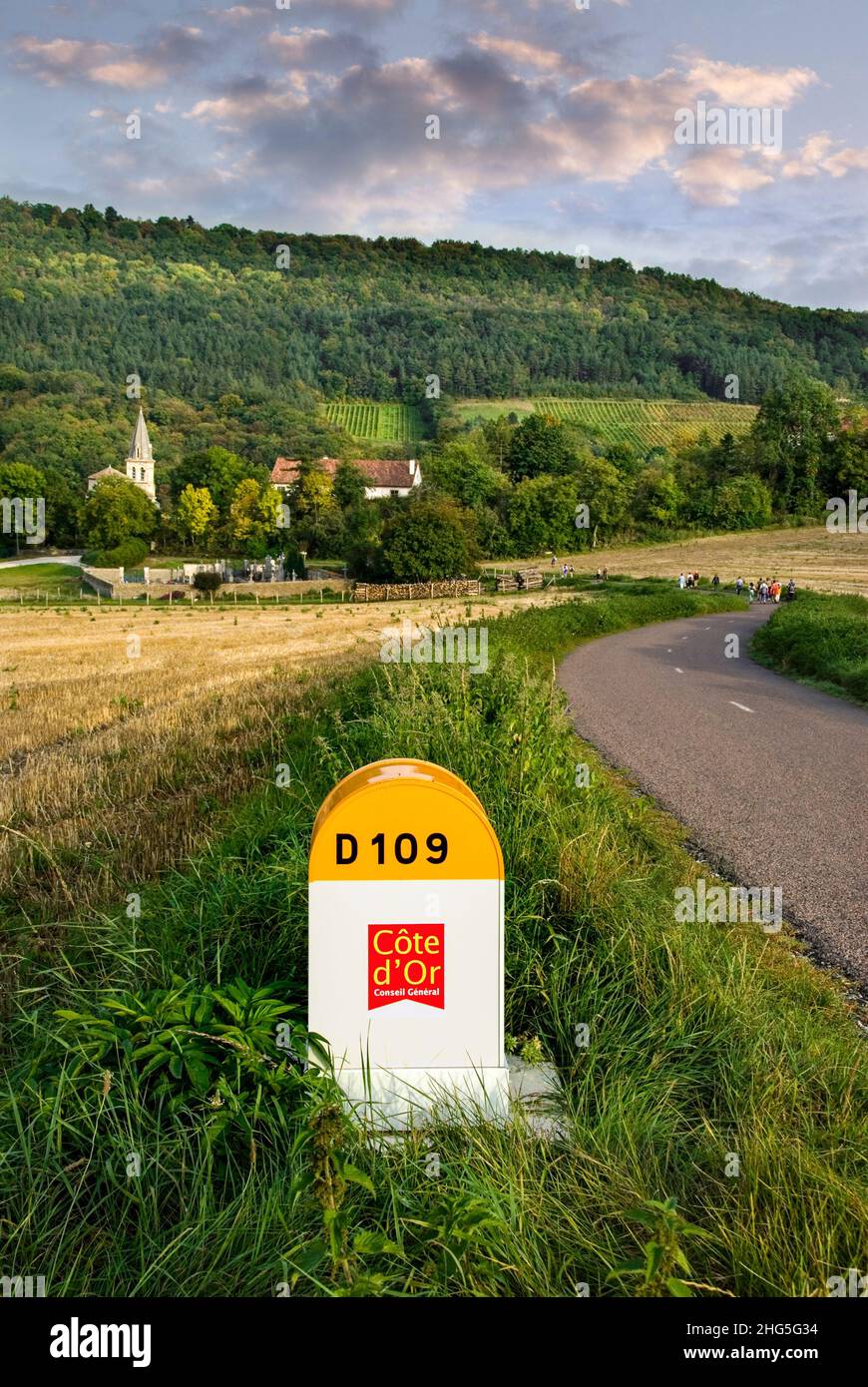 Hautes Cotes de Nuits carretera rural señal D109 poste marcador, piedra de carretera y Curtil-Vergy pueblo detrás con caminantes, Cote d'Or, Borgoña Francia Foto de stock