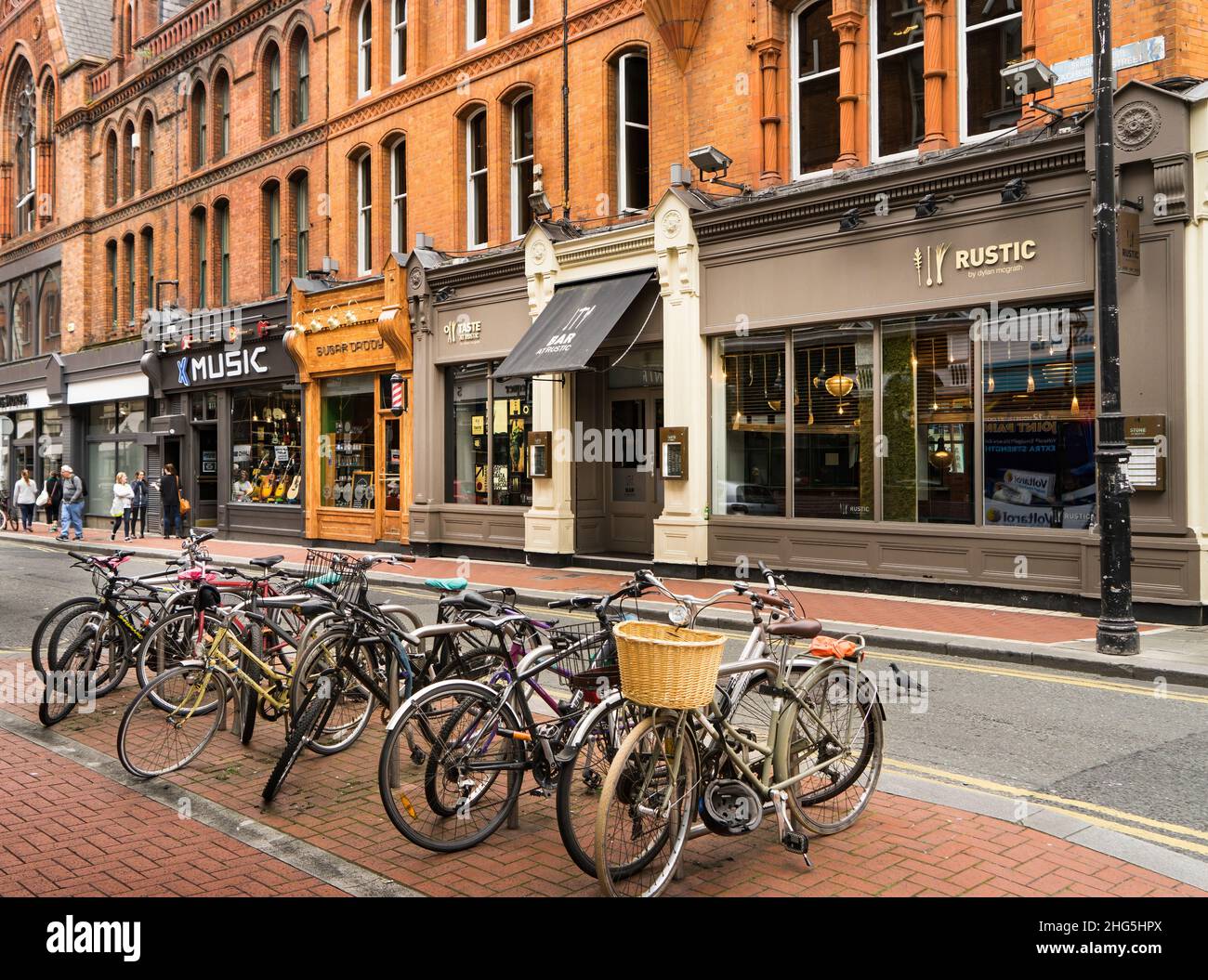 Calle comercial en Dublín, con un grupo de bicicletas en primer plano y un edificio con tiendas en el fondo. Foto de stock