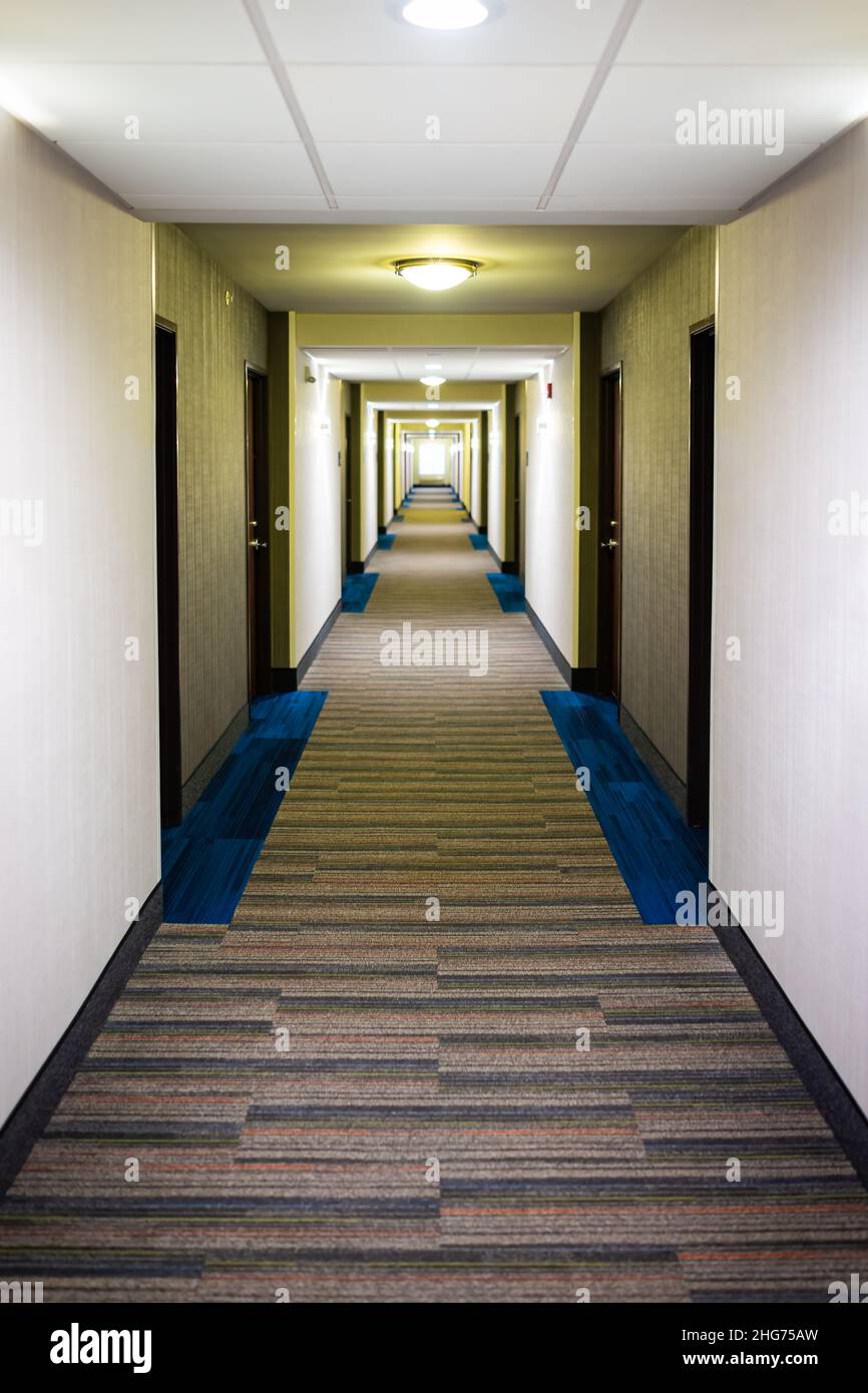 Moderno hotel motel motel pasillo largo vacío con diseño de suelo de moqueta y luces iluminado interior vertical vista de la arquitectura del edificio Foto de stock