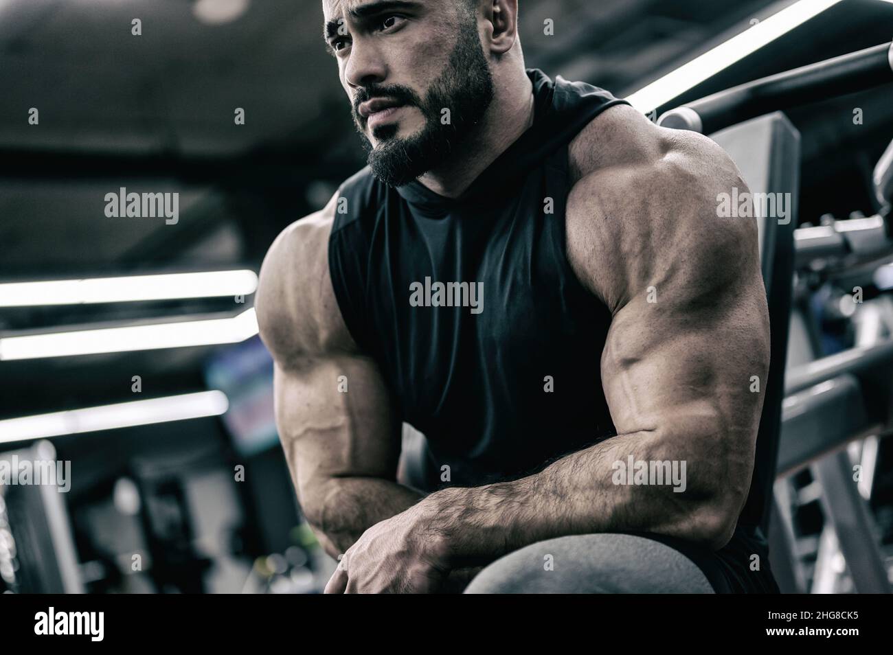 hombre fuerte y joven con barba sentado en el gimnasio deportivo durante el tiempo de relajación en el entrenamiento de fitness muscular Foto de stock