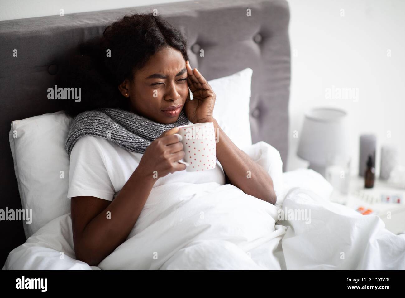 Dama negra acostada en la cama con una taza de bebida caliente Foto de stock