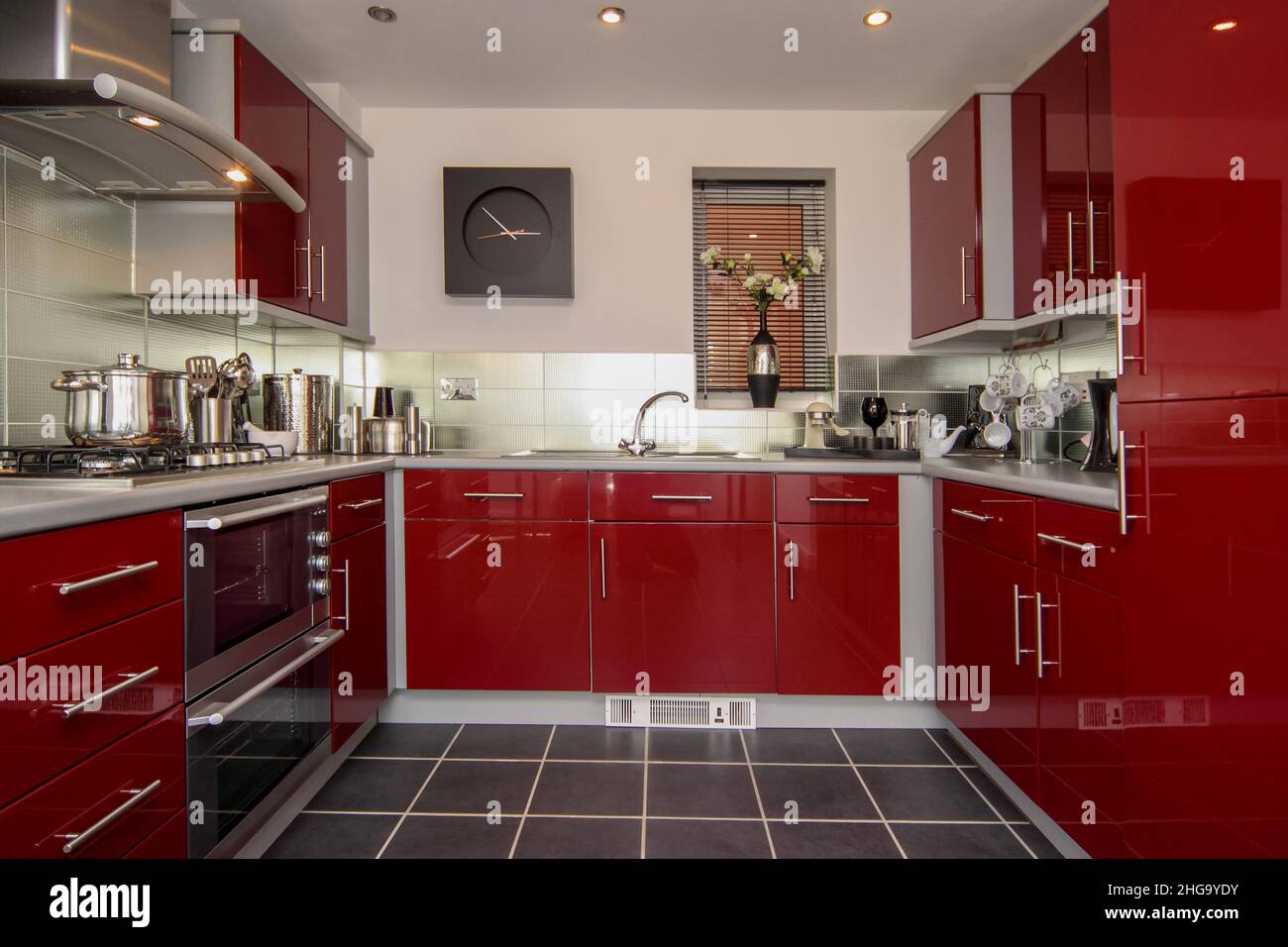 Cocina moderna, unidades de alto brillo rojo oscuro, reloj de pared, suelo de baldosa, acero inoxidable Foto de stock