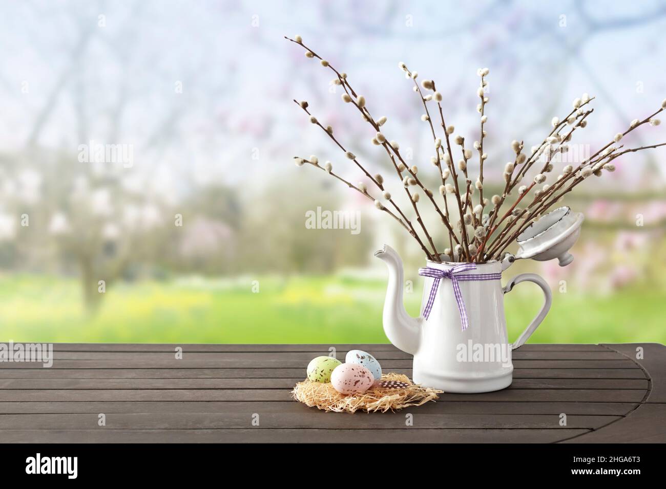 Huevos de Pascua en colores suaves en un nido con el coño willow ramitas una jarra blanca, contra un fondo de jardín de primavera, espacio de copia para el texto Feliz Pascua. Foto de stock