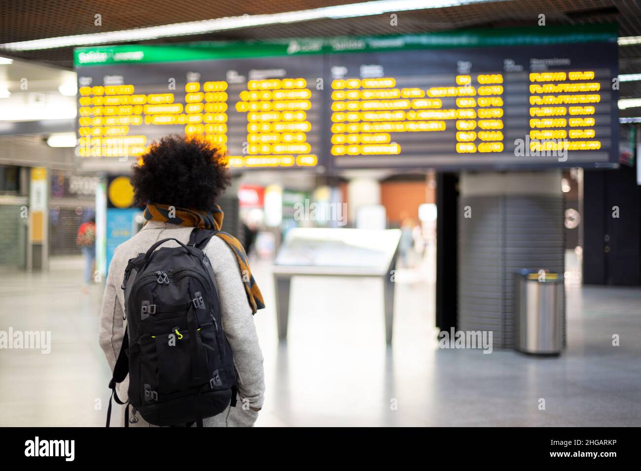 Viajero joven que mira las salidas y el panel de llegadas en el aeropuerto o la estación de tren. Espacio para texto. Foto de stock