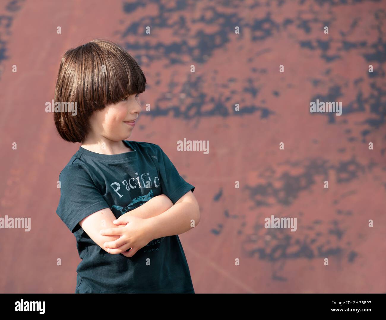 El niño sonríe y cruza las manos en el pecho, retrato Foto de stock