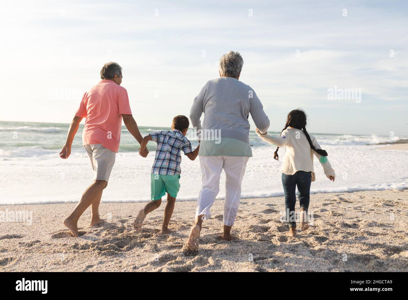 Vista trasera de abuelos multirraciales mayores caminando con nietos en la playa Foto de stock