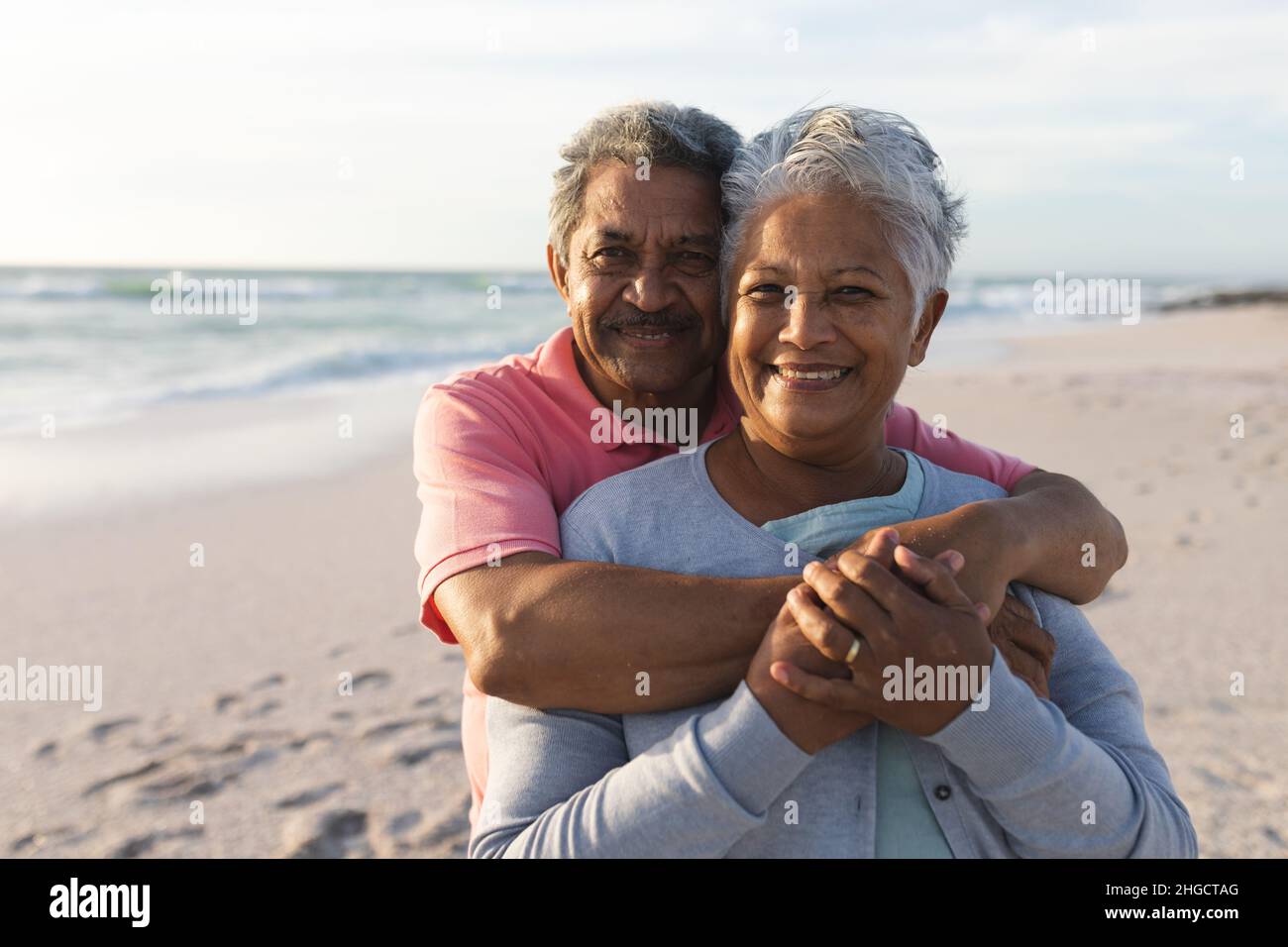 Retrato de un hombre de edad avanzada cariñosa abrazando a una mujer desde atrás en la playa durante la puesta de sol Foto de stock