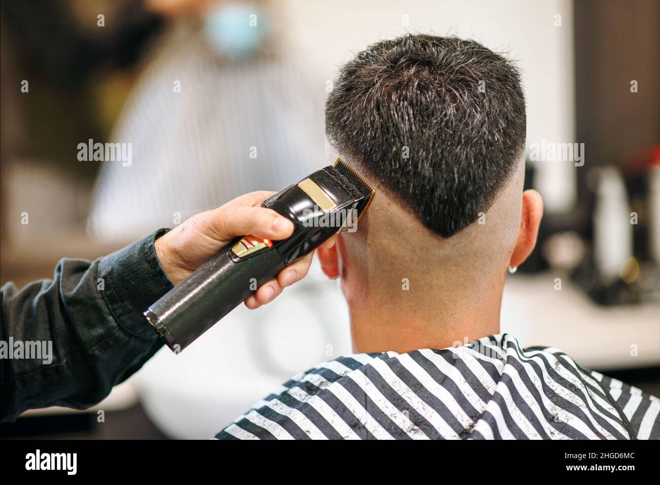 Barbero profesional que utiliza una afeitadora eléctrica o un cortapatillas  para enconar el peinado moderno en forma de V de un cliente masculino visto  desde la parte trasera en primer plano Fotografía