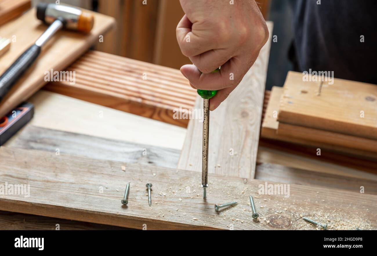 Herramienta manual de destornillador, tornillo manual macho en madera. Vista de primer plano de la mesa de trabajo de carpintero. Bricolaje, reparación y reparación en casa. Foto de stock