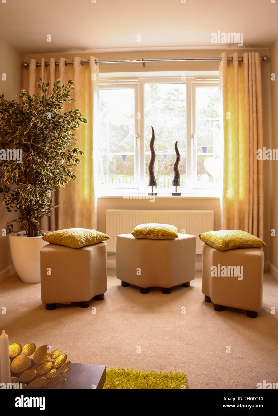 Tres taburetes de pouffe de color crema con cojines dorados en una moderna sala de estar Foto de stock