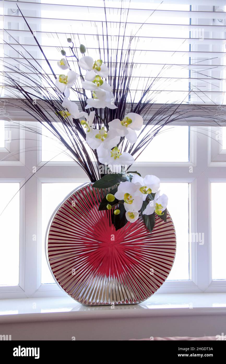 Moderno jarrón cromado reflectante con flores blancas como orquídeas en un borde de ventana, estilo de vida, estilo. Foto de stock