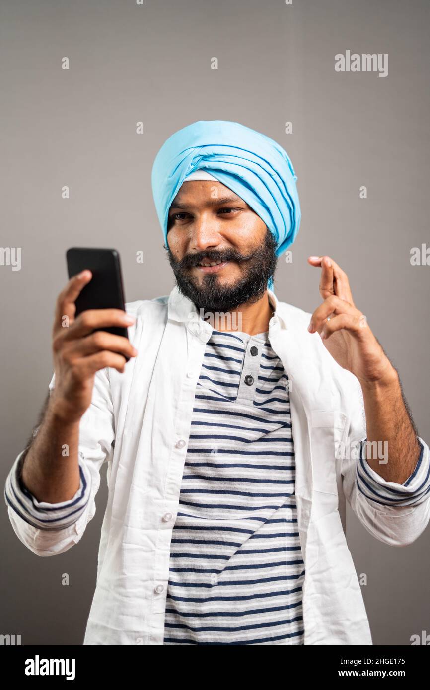 Concepto de wating para la promoción del trabajo, lotería o resultados de la entrevista que muestra el hombre joven sikh tensado usando el teléfono móvil en el fondo del estudio. Foto de stock