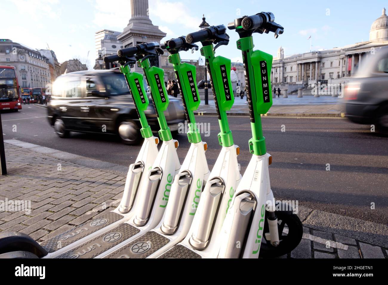 Los vehículos pasan una fila de scooters eléctricos para alquilar estacionados en la bahía dedicada, en el centro de Londres, Reino Unido Foto de stock