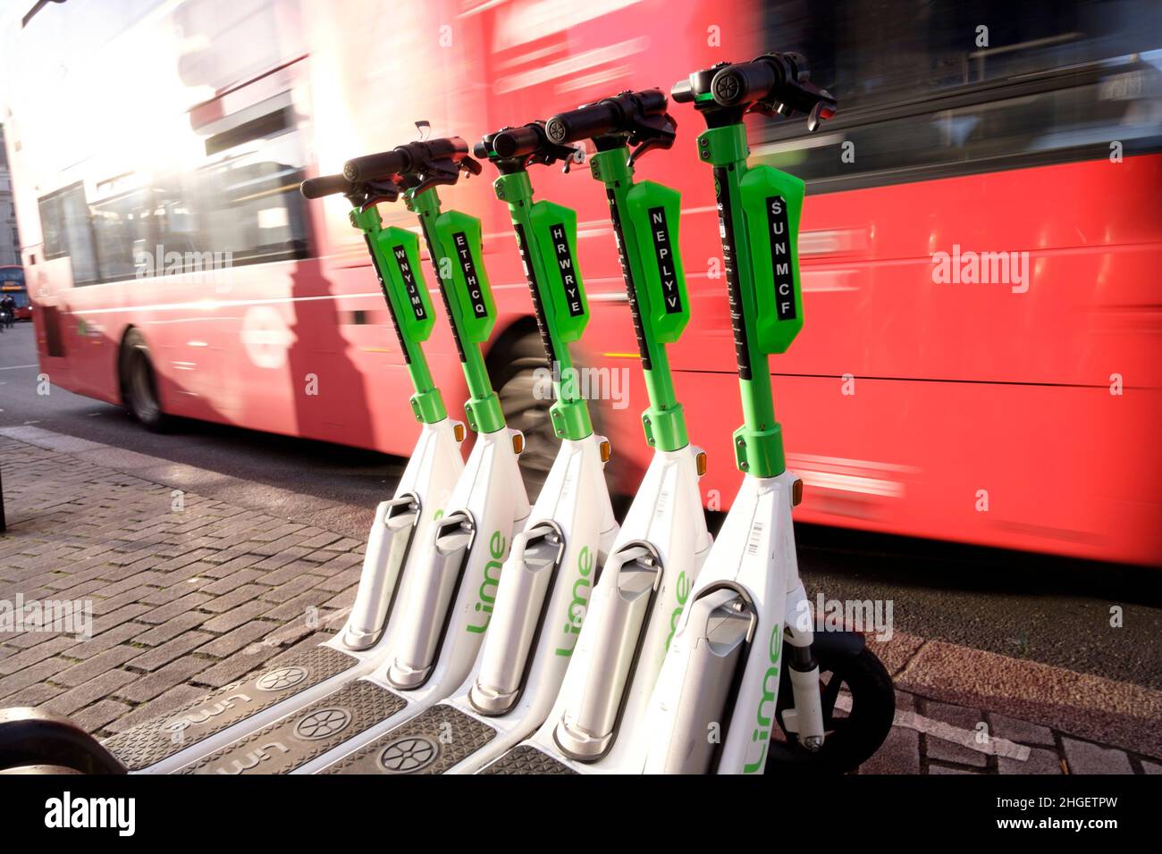 Un autobús de Londres pasa una fila de scooters eléctricos para alquilar estacionados en la bahía dedicada, en el centro de Londres, Reino Unido Foto de stock