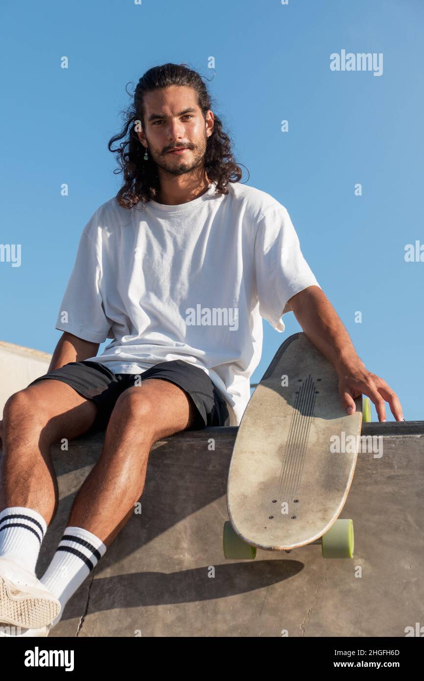 Retrato de skater para adultos jóvenes de pie al aire libre sosteniendo su  skateboard. Tiene un largo cabello negro y una barba Fotografía de stock -  Alamy