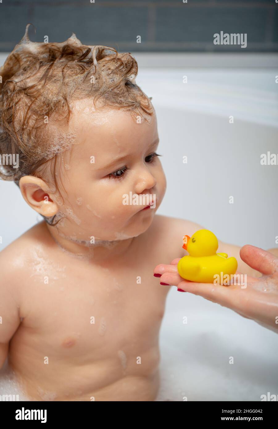 Baño de burbujas para niños. Feliz bebé tomando un baño jugando con burbujas espuma. Niño pequeño en la bañera. Niño sonriente en el baño con pato de juguete. Bebé Fotografía de
