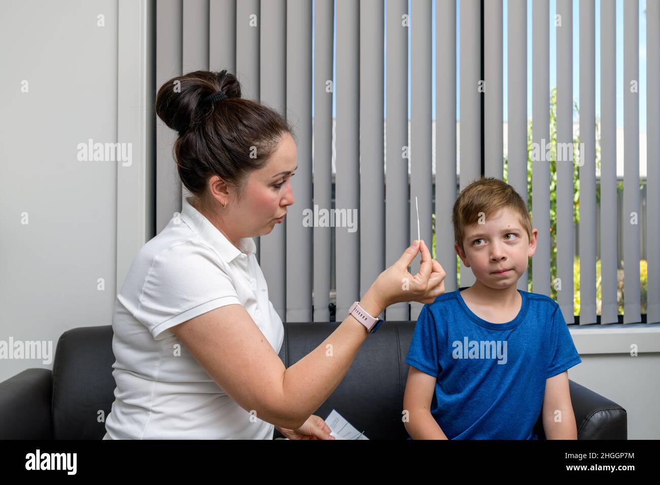 Madre va a hacer la prueba rápida de antígeno COVID-19 para su hijo mostrándole un hisopo Foto de stock