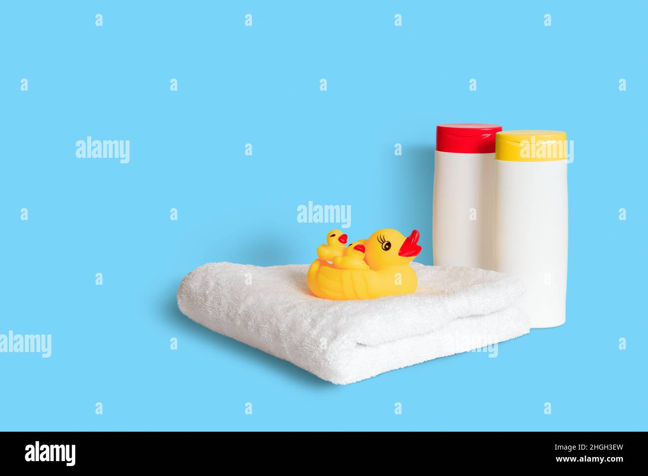 Pato de goma amarillo sobre toalla blanca suave y dos botellas blancas de  plástico con tapones amarillos y rojos sobre fondo azul claro. Accesorios  de baño para niños Fotografía de stock -