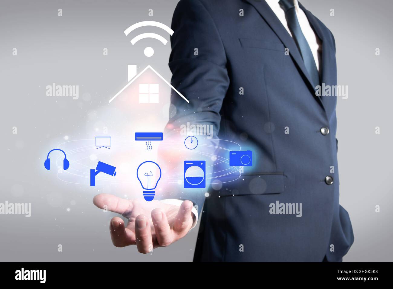 Hombre en la chaqueta sosteniendo una casa conectada por wi-fi a diferentes dispositivos electrónicos. Automatización del hogar en el hogar Foto de stock