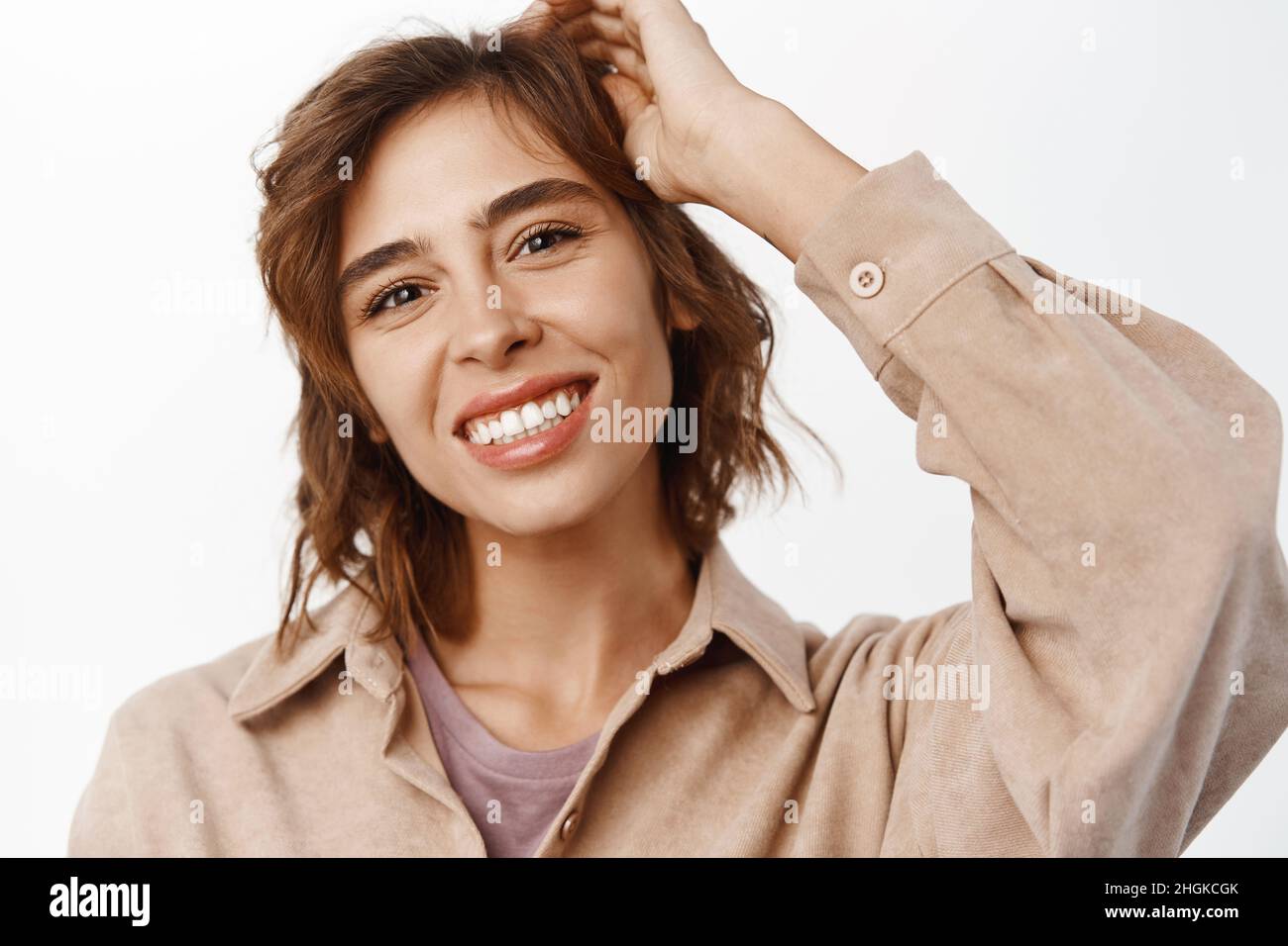 Belleza. Mujer joven femenina con peinado corto rizado, sonrisa blanca,  piel clara natural sin manchas o acné, tocando su cara y mirando Fotografía  de stock - Alamy
