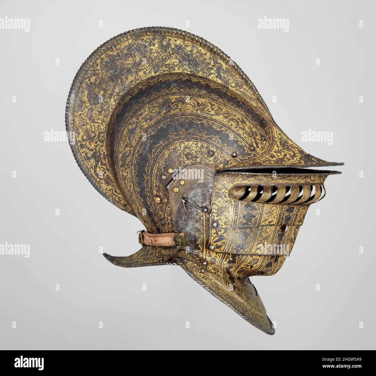 Burgonet con Buffe ca. 1555–60 Italiano La forma elegante y la hermosa decoración de este casco sugieren que fue hecho en Italia bajo influencia francesa. El excepcionalmente alto y retrógrado peine a lo largo de la parte superior del casco, la forma y el apego del búfalo (defensa de la cara), y los finos rollos que bordean las bandas grabadas son todas características de la armadura francesa en el 1550s. Sin embargo, el estilo del grabado y la elección de motivos –trofeos ampliamente espaciados de armadura, armas y símbolos clásicos– son más típicos de la mejor armadura italiana de la época. Burgonet con Buffe. Italiano. c Foto de stock