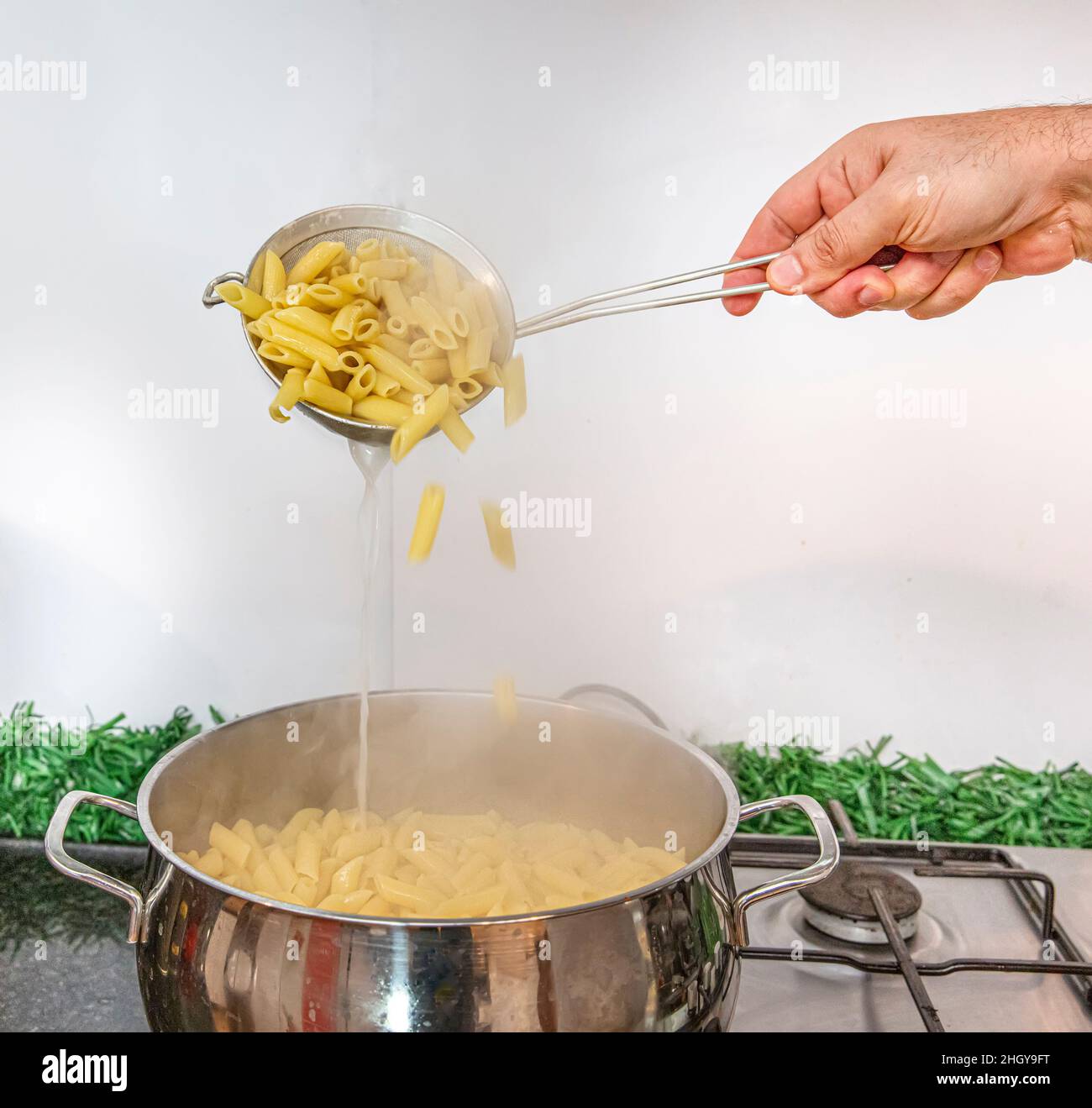 Cooking Pasta Pour the penne pasta en una olla de metal de agua hirviendo.  Penne hervida en un colador de acero, en una clase de cocina Fotografía de  stock - Alamy