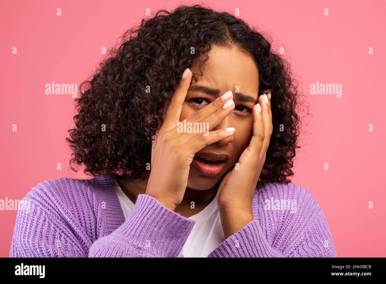 Concepto de emociones humanas negativas. Joven mujer negra que se siente asustada, cubriendo su cara en pánico sobre el fondo rosa del estudio Foto de stock