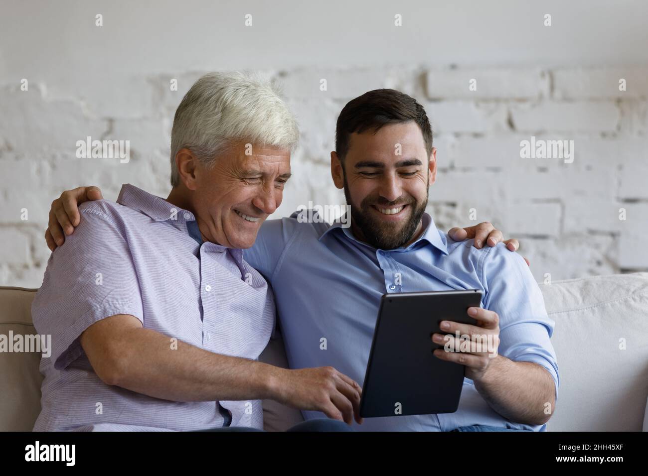 Feliz hijo adulto enseñando a padre maduro a utilizar la aplicación en línea Foto de stock