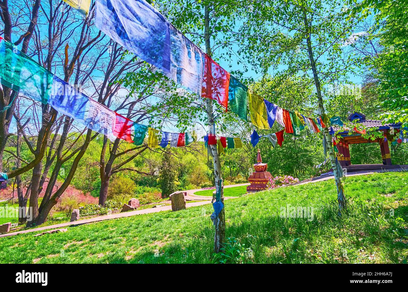 Pasee por el sombrío glade del Jardín Tibetano con una vista sobre los abedules delgados, las banderas de oración colgadas y el Chorten Tibetano en el fondo, el Jardín Botánico de Kiev Foto de stock