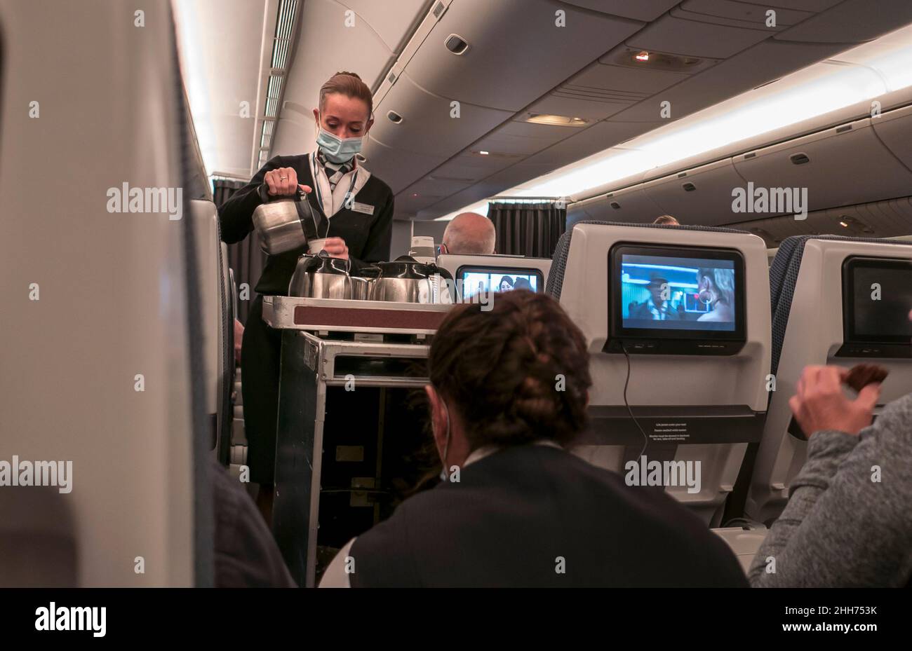 Azafata con máscara facial Covid que sirve a los clientes en el avión. Foto de stock