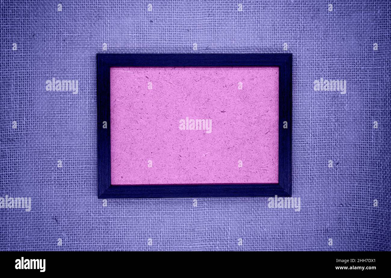 Burla, composición abstracta. Marco de madera sobre burlap púrpura. Dentro del marco hay una base texturizada en rosa. Colores 2022 (muy peri) Foto de stock