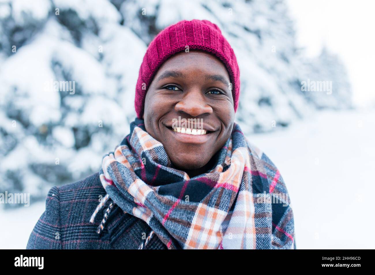 hombre de mano afroamericano con sombrero rojo y elegante abrigo a cuadros mirar la cámara con una sonrisa blanca de nieve enana al aire libre en el parque Foto de stock