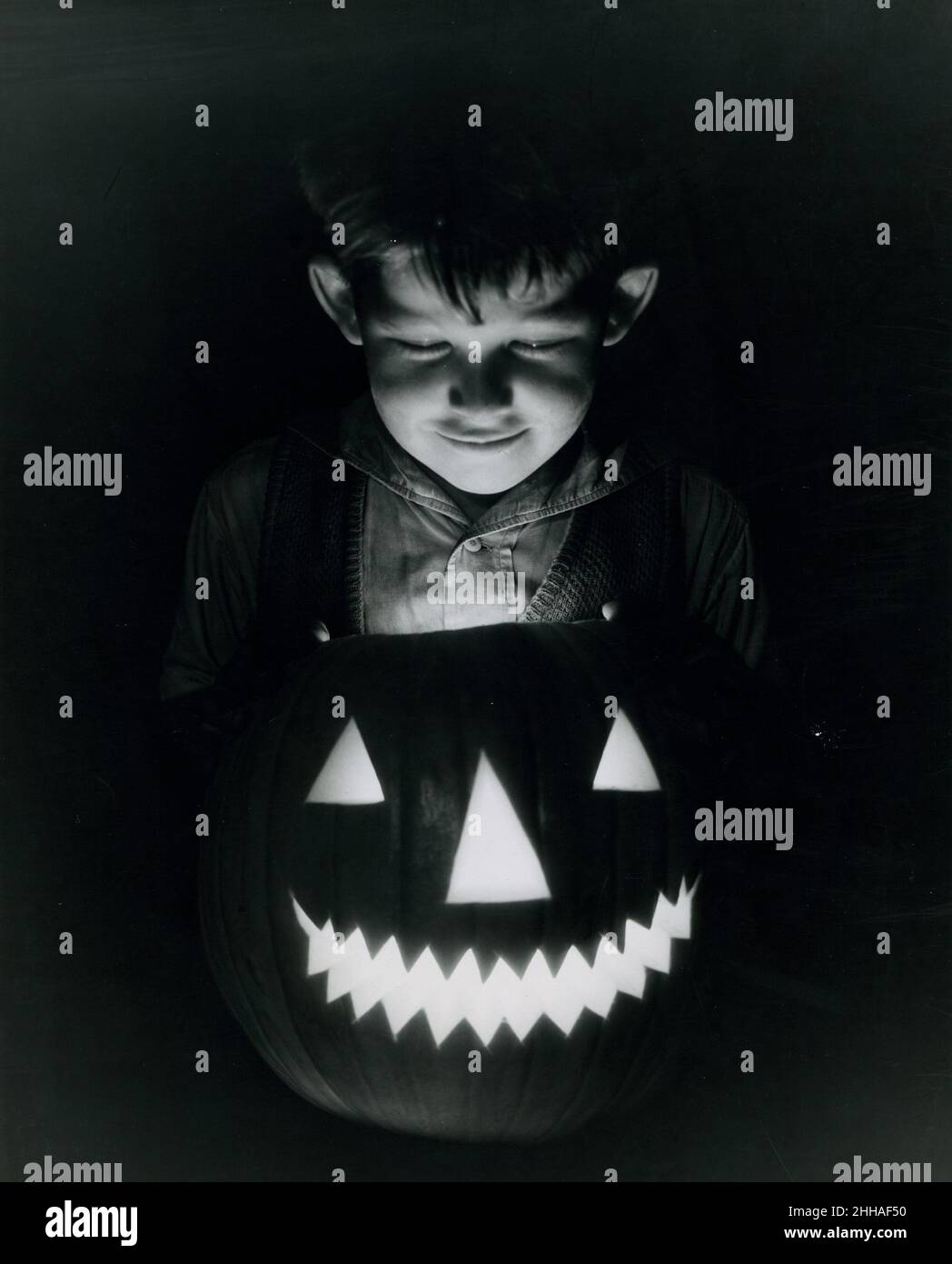 1940's - Un niño pequeño se refleja en el brillo espeluznante de su linterna de Halloween Jack o'. Foto de stock