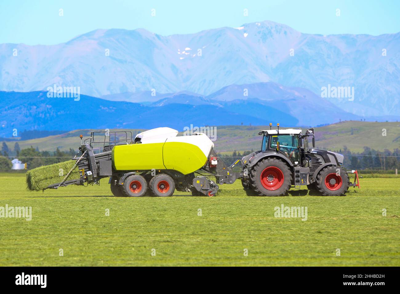 Un tractor y un enfardador de heno trabajando en un campo de granja en la zona rural de Canterbury, Nueva Zelanda Foto de stock